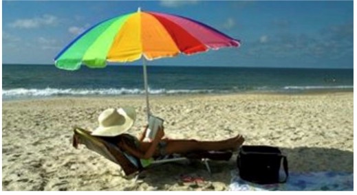 Lady reading on the beach under an umbrella.